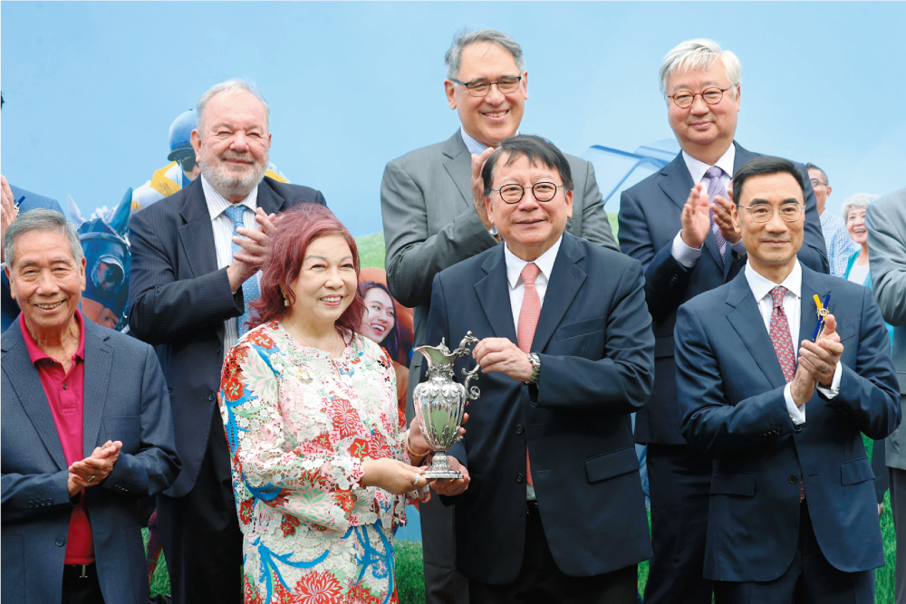 香港特別行政區政府政務司司長陳國基（前排右二）於「香港賽馬會社群盃」賽事後，頒發獎盃予頭馬萬事快的馬主伍燕梅（前排左二）。賽事頒發的獎盃已有超過一百七十年歷史，由收藏家雷剛先生捐贈，以表揚馬會對社會的貢獻。