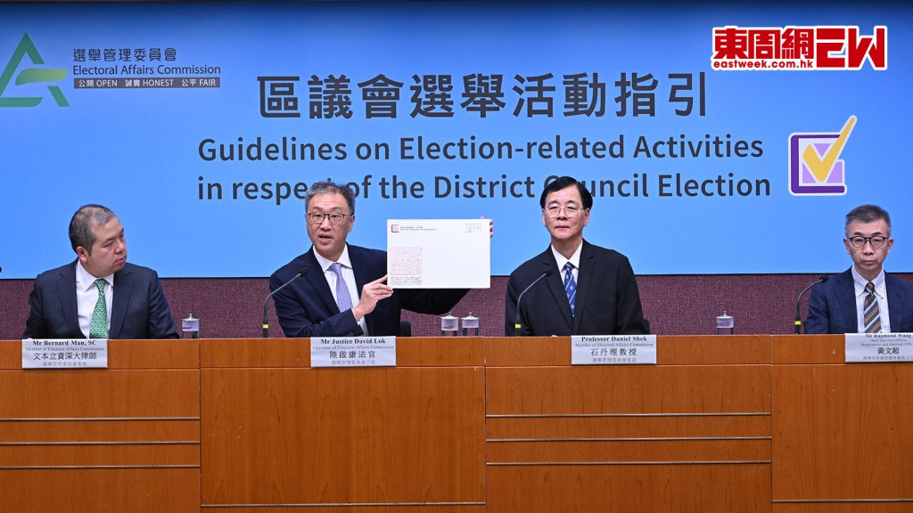區議會選舉十二月十日舉行,選舉管理委員會主席陸啟康(中)早前講解活動指引,展示投票寄給地區委員會界別選民的投票通知卡信封樣本。