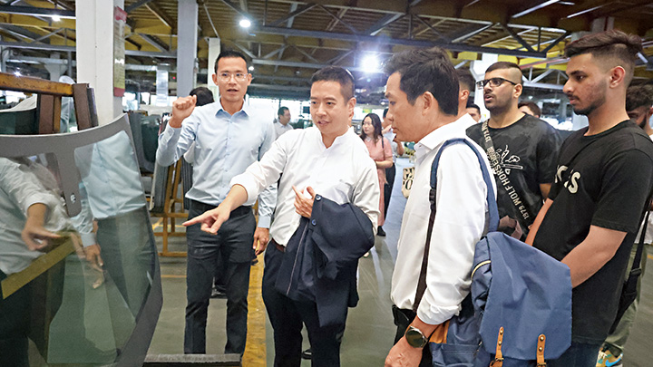 信義玻璃執行董事李聖根 （左一）向油尖旺民政事務專員余健強（中）及少數族裔青年解說玻璃生產的過程。