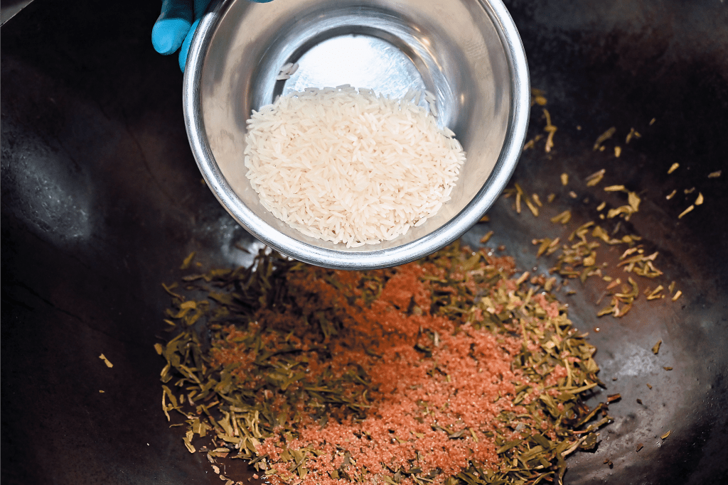  2. 在白鑊中按次序加入茶葉、黑糖拌勻，再鋪上白米，慢火加熱炒至滲出香味及微微焦黃。