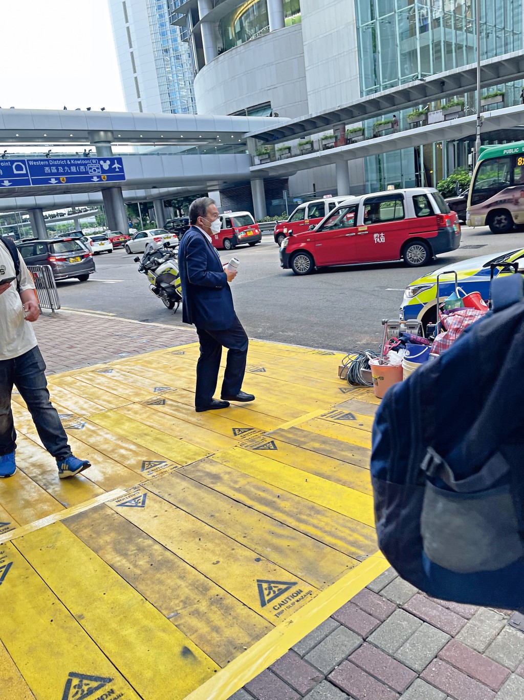  手持空氣淨化機的胡定旭，站在街頭一邊等車、一邊低着頭睇電話。