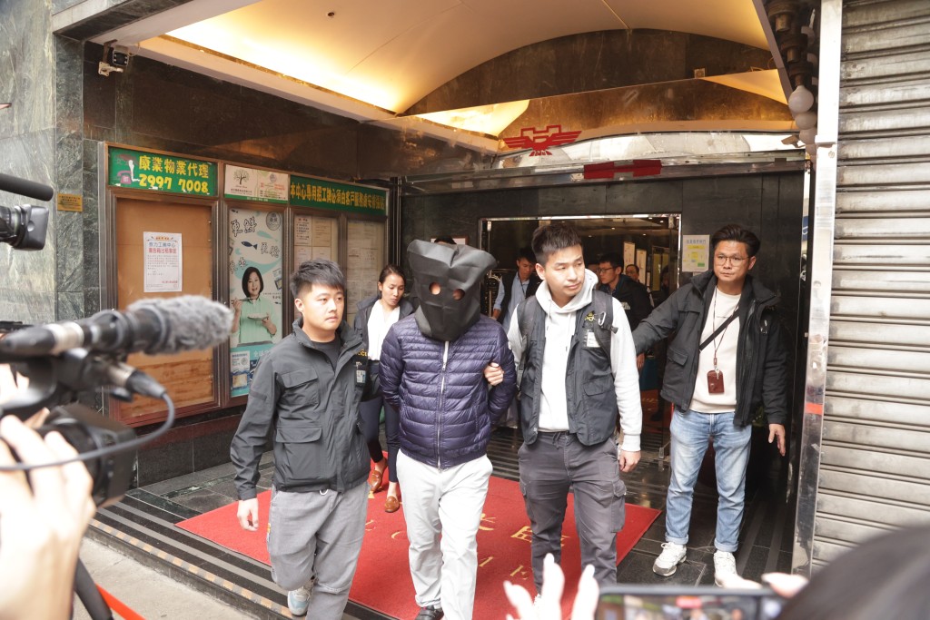 被警方拘捕的「宏業」負責人以黑布蒙頭，被警員帶走。
